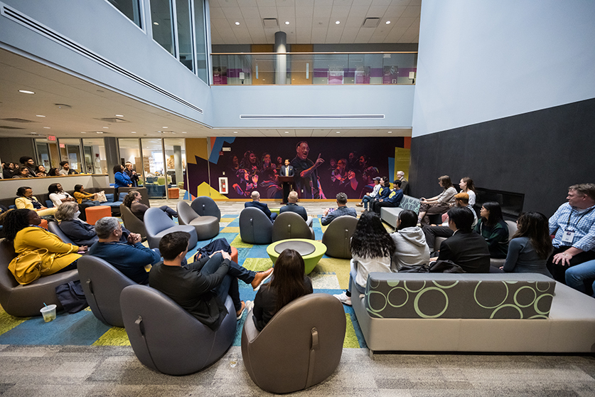 An atrium in the center with people listening to a speaker.