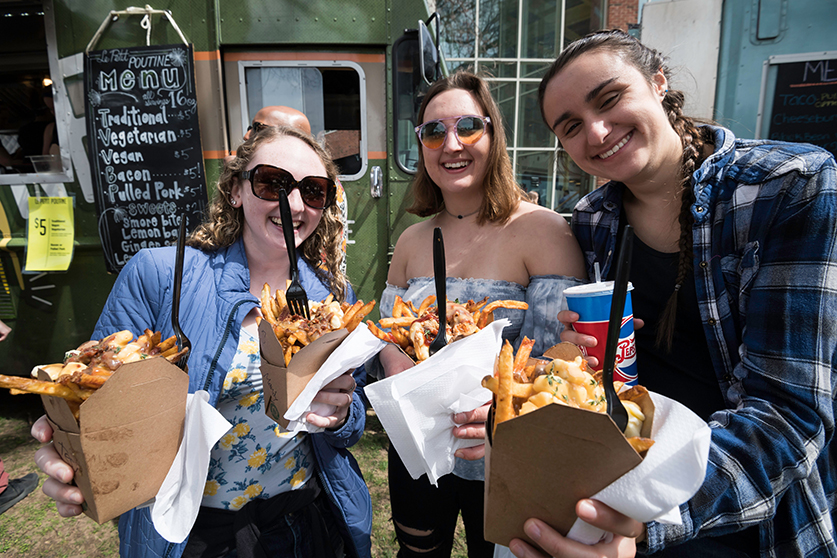 A group of students holding out their recent food truck purchase towards the camera.