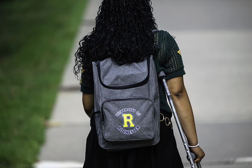 A student shown from behind with a Rochester backpack and a crutch.